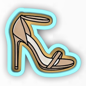 May include: A cookie cutter in the shape of a high-heeled sandal. The cutter is made of light blue plastic and has a gold outline. The sandal is beige with a brown strap.