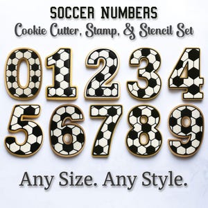 May include: A set of cookie cutters, stamps, and stencils in the shape of soccer ball-patterned numbers 0 through 9. The numbers are black and white with a gold border. The text "SOCCER NUMBERS" and "Any Size. Any Style." are also visible.