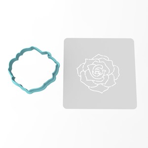 May include: A light blue plastic cookie cutter shaped like a rose, next to a white stencil of a rose on a gray background.