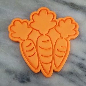 May include: Orange plastic cookie cutter shaped like three carrots with green tops.