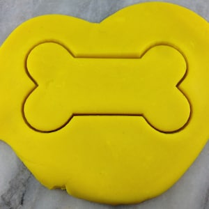 以下が含まれることがあります： 骨の形をした黄色のクッキーカッター。カッターは黄色の表面の上に置かれています。