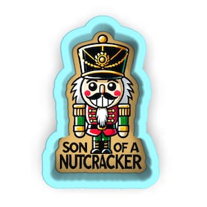 Peut inclure: Un dessin de casse-noisette de style cartoon avec un contour bleu clair. Le casse-noisette porte un chapeau noir avec des bordures dorées, une veste rouge et des accents verts. Le texte "SON OF A NUTCRACKER" est affiché.