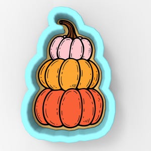 May include: A stacked pumpkin cookie cutter with a light blue outline. The pumpkins are in shades of pink, orange, and red-orange, with a brown stem. The design is a whimsical representation of autumn and fall.