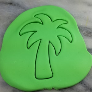 Puede incluir: Un cortador de galletas verde en forma de palmera. El cortador está sobre una superficie verde.