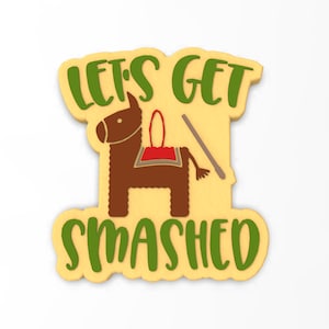 May include: A yellow cookie decorated with green icing and the text "Let's Get Smashed". A brown donkey piñata with a red saddle and a stick is in the centre of the cookie.