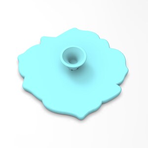 May include: A light blue silicone phone stand shaped like a flower with a raised center. The stand has a smooth, matte finish.