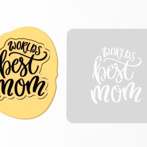 May include: A white stencil with the text "World's Best Mom" in black lettering. The stencil is on a gray background.