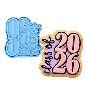 May include: A light blue plastic cookie cutter next to a decorated cookie. The cookie is shaped with the words "Class of 2026" in black and pink icing. The cookie has a light purple background.