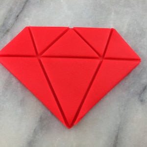 May include: A red diamond-shaped fondant decoration, divided into smaller triangles, for a cake or other dessert.