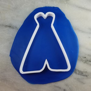 May include: A white plastic cookie cutter in the shape of a dress on a blue background.
