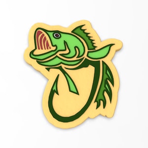 Puede incluir: Un anzuelo de pesca verde y amarillo con un pez verde en él. El pez tiene un ojo rojo y la boca abierta.
