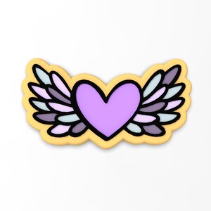 May include: A yellow cookie with a purple heart and white and purple wings. The heart has a black outline and the wings have a black outline and a white outline.