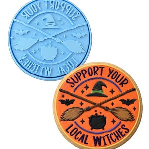 May include: A light blue circular cookie stamp featuring a witch hat, crossed broomsticks, a cauldron, bats, and stars with the text SUPPORT YOUR LOCAL WITCHES, alongside a round cookie decorated with orange icing and matching black and brown details.