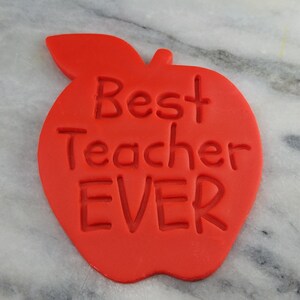 Peut inclure: Emporte-pièce en forme de pomme rouge avec les mots "Best Teacher Ever" en relief sur le devant.