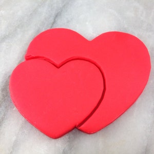 Pode incluir: Dois cortadores de biscoitos em forma de coração vermelho, um aninhado dentro do outro.