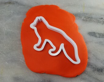 May include: A white plastic fox-shaped cookie cutter on a bright orange surface. The cutter's outline clearly defines the fox's form, with its pointed ears and bushy tail. The orange surface provides a vibrant contrast.