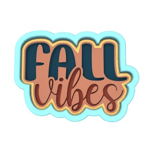 Op de afbeelding: Een gelaagd papieren uitsnijwerk in blauw, geel en bruin met de tekst "Fall vibes".
