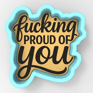 May include: A cookie cutter with the words "fucking PROUD OF you" in black script and block letters. The text is on a gold background, framed by a light blue border. The design is on a white surface.