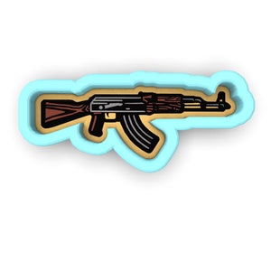 May include: A blue plastic cookie cutter shaped like an AK-47 assault rifle.