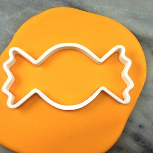 May include: A white plastic candy cookie cutter on a bright orange surface.