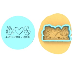 Op de afbeelding: Een blauwe koekjesvormer met de tekst "Peace Love Fall" en afbeeldingen van een vredesteken, een hart en een pompoen.