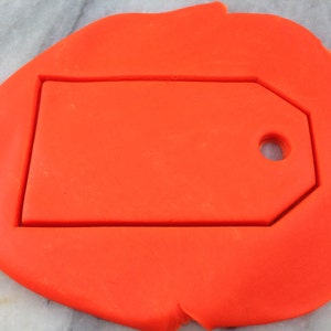 Könnte beinhalten: Orangener Fondant mit einem ausgeschnittenen Etikett. Das Etikett hat oben ein Loch.