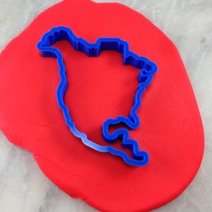 K&ouml;nnte beinhalten: Ein blauer Plastik-Ausstecher in Form des nordamerikanischen Kontinents, der in roten Modellierton gedr&uuml;ckt wird.