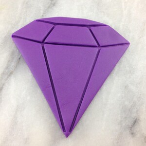 Op de afbeelding: Een paarse diamantvormige fondant-uitsnijding, perfect voor het decoreren van taarten of cupcakes.