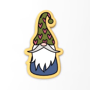 May include: A yellow gingerbread cookie shaped like a gnome with a green hat with pink hearts, a white beard, and a blue shirt.
