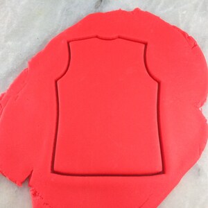 May include: Red fondant with a sleeveless shirt cookie cutter pressed into it.