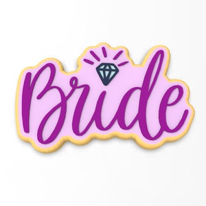 以下が含まれることがあります： ピンクとパープルのクッキーで、「Bride」という言葉とダイヤモンドのグラフィックが飾られています。