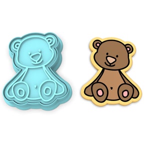 K&ouml;nnte beinhalten: Ein blauer Plastik-Ausstecher in Form eines Teddyb&auml;ren, neben einem braunen Zuckerkeks in Form eines Teddyb&auml;ren.