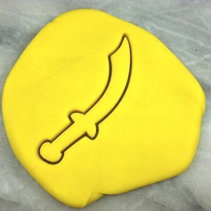 May include: A yellow fondant cookie dough with a cutout of a black sword shape.