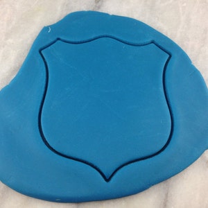Op de afbeelding: Een blauwe fondant-uitsnede in de vorm van een schild, klaar om te decoreren.