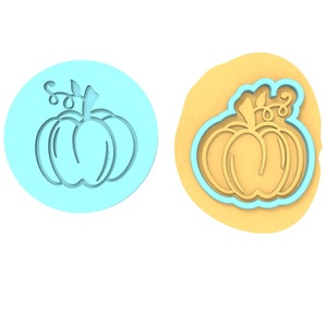 May include: A blue plastic pumpkin cookie cutter with a yellow pumpkin cookie on a yellow background.