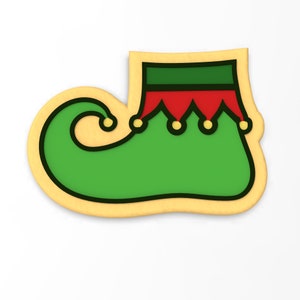 May include: A green and red elf shoe cookie cutter. The cookie cutter is shaped like a shoe with a pointed toe and a curved heel. The shoe has a green body, a red cuff, and a yellow buckle.
