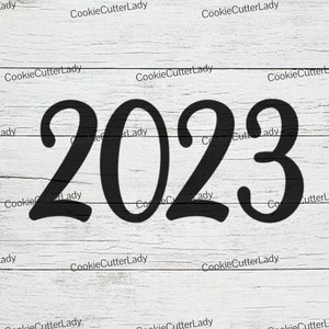 May include: Black and white image of the year 2023 written in a stylized script font on a white wood background.