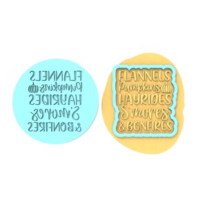 Op de afbeelding: Twee koekjesvormen, een ronde en een vierkante, met de tekst "FLANNELS, Pumpkins, HAYRIDES, S'mores, & BONFIRES" in een blauwe omtrek op een beige achtergrond.