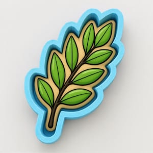 May include: A light blue cookie cutter shaped like a leafy branch. Inside the cutter is a tan cookie decorated with a dark brown stem and six bright green leaves. The design features a clear outline of the branch shape with defined leaf veins.