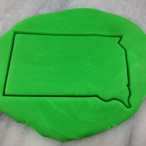 May include: A green cookie cutter in the shape of the state of North Dakota.