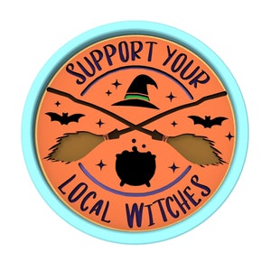 May include: A round, orange and blue sign with the text "Support Your Local Witches" in a black and purple font. The sign features a black witch's hat, two crossed broomsticks, and a black cauldron.