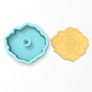 May include: A light blue plastic cookie cutter shaped like a rose. The cutter is shown next to a yellow cookie that has been cut out using the cutter.