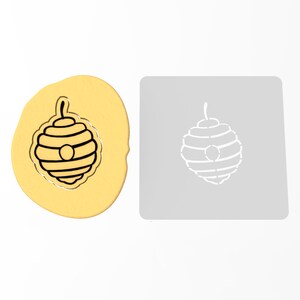 May include: A cookie cutter and a piece of cookie dough, both shaped like a beehive with a round opening at the top.