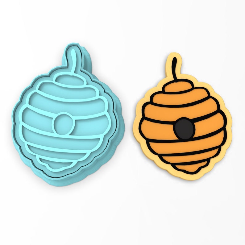 May include: A blue plastic cookie cutter shaped like a beehive, next to a yellow cookie decorated with black icing to look like a beehive.