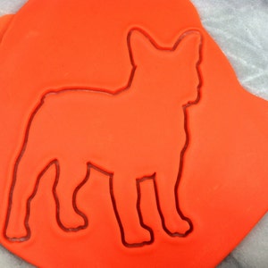 Puede incluir: Masa de galleta naranja con un cortador de galletas con forma de bulldog francés presionado en ella.