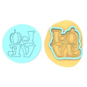 Op de afbeelding: Een blauwe en witte koekjesvormer met het woord "LOVE" en een pompoenontwerp. De vormer wordt getoond naast een geel koekdeeg.