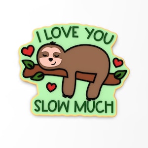 May include: A green and brown cookie with a cartoon sloth sleeping on a branch. The cookie has the text "I love you slow much" on it.