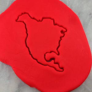K&ouml;nnte beinhalten: Roter Keksteig mit einem in ihn gepressten Keksausstecher in Form von Nordamerika.