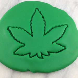 Könnte beinhalten: Grüner Fondant mit einem Ausstecher in Form eines Cannabisblattes.