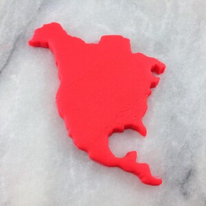 K&ouml;nnte beinhalten: Ein roter Playdough-Ausschnitt des nordamerikanischen Kontinents auf einer wei&szlig;en Marmorfl&auml;che.